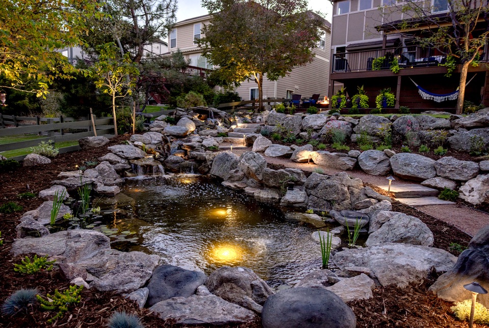 Lit pond and lawn at dusk, house behind