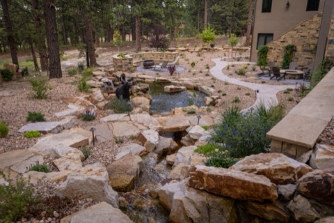 A beautiful backyard landscape with gravel, ponds, waterfalls, winding sidewalks and rock work in the forest