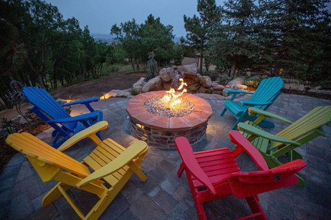 Colourful Adirondack chairs around a round fire pit under pines