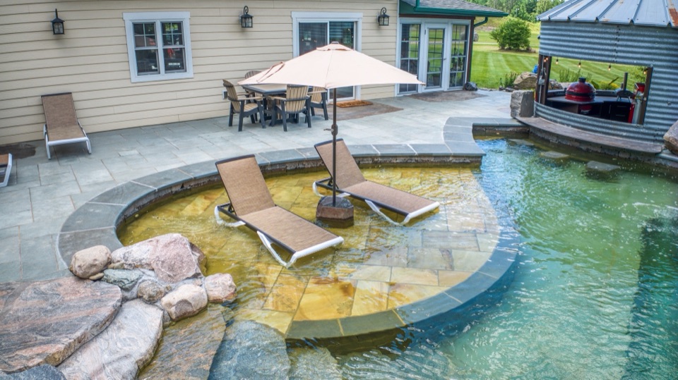 Natural pool with sun shelf and lounge chairs by the house