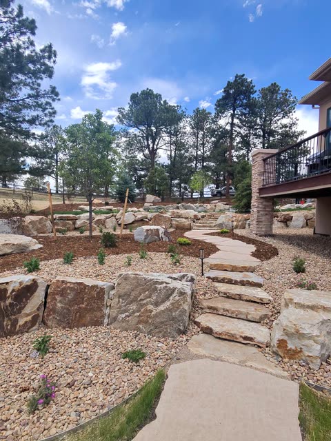 Flagstone steps climbing between boulder walls, river rock and low-water plantings under tall pines