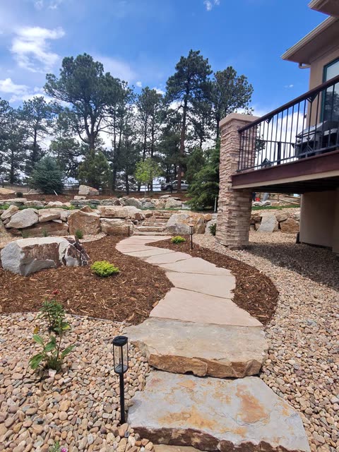 Flagstone path through mulch beds and river rock beside a deck, with path lights
