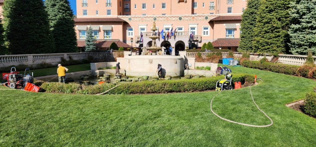 A team of pond professionals cleans a large water feature in front of a historic hotel